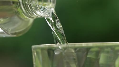 Clear Liquid Pouring from Bottle to Glass Outdoors