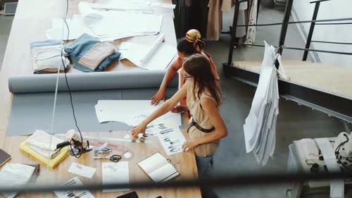High Angle of Two Female Tailors Discussing Fashion Sketches in Studio