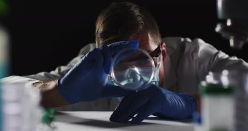 Caucasian male doctor wearing face mask and gloves inspecting petri dish