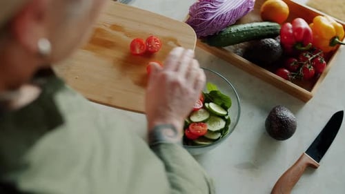Top View of Lady's Hand Putting Juicy Tomatoes in Bowl with Vegetable Salad Making Lunch at Home