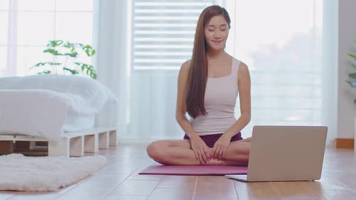 Athlete Asian woman looking laptop practice yoga lotus pose online course at home to meditation