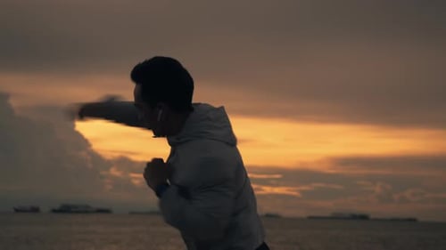 Silhouette of a boxer Asian man is practicing boxing workout on the beach.
