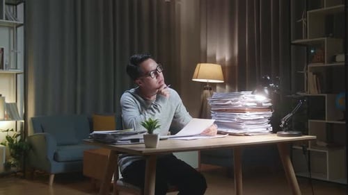 Adult Reviews Paperwork at Desk at Night