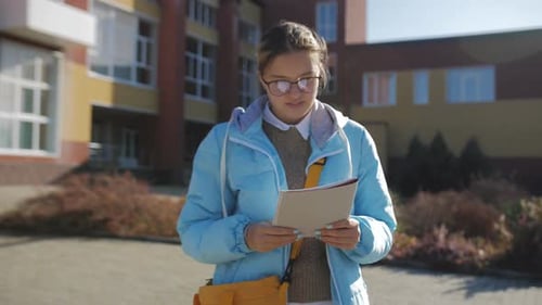 Teenage Girl Reads Notebook Outside School on Sunny Day