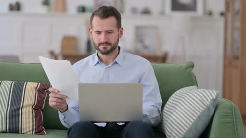 Focused Man Working with Laptop and Documents at Home