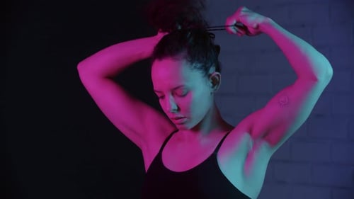 Woman Puts Hair Up in Ponytail with Neon Lighting