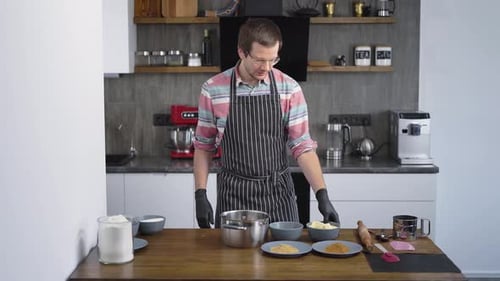 A Young Nice Chef Is a Man in the Kitchen. The Confectioner Mixes the Ingredients for the Dough in