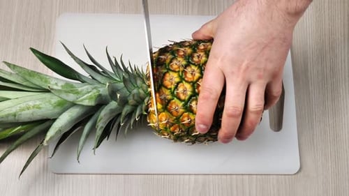 Hands Trim Fresh Pineapple on Cutting Board