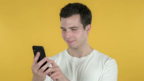 Young Man Using Mobile Phone Against Yellow Background