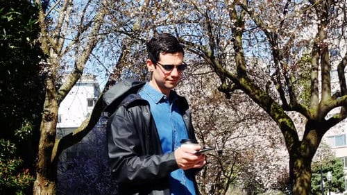 Man using mobile phone while having coffee in park 4k