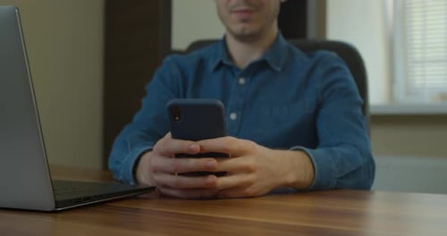 Mann sitzt an seinem Schreibtisch zu Hause am Desktop-Computer. Beginnt mit der Nutzung des Smartphones, verwendet die Social Media App
