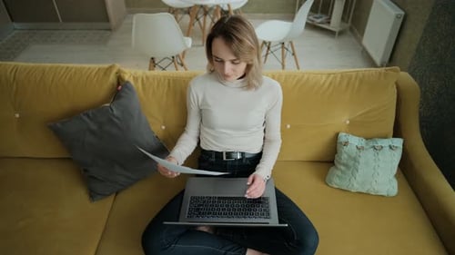 Woman Analyzes Paperwork and Types on Laptop at Home