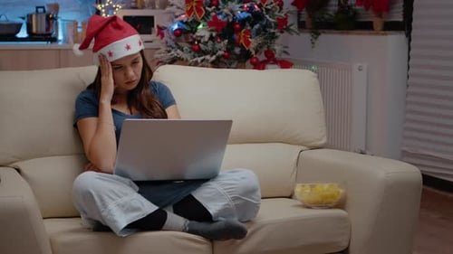 Woman Wearing Santa Hat Uses Laptop at Home