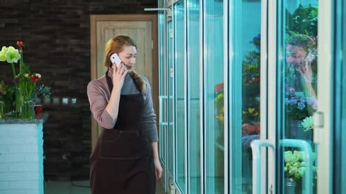 The Owner of the Flower Shop Talking on the Phone and Walks Looking Showcase of Flowers