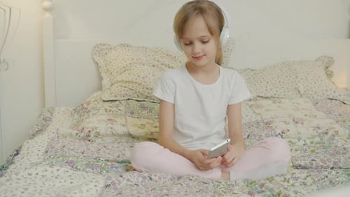 Young Girl Using Phone With Headphones on Bed