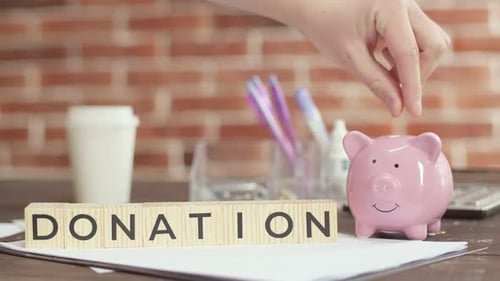 Die Spende ist auf Holzwürfel geschrieben, die auf dem Schreibtisch liegen. Hand legt Geld ins Sparschwein.