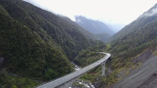 Imagen de
rastreo aéreo de coches en una carretera con bosque montañoso y acantilado rocoso.
