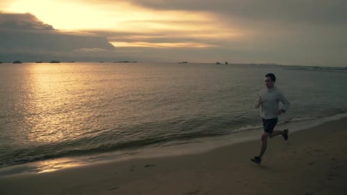 Asian sportsman running on the beach during a beautiful sunset in summer.