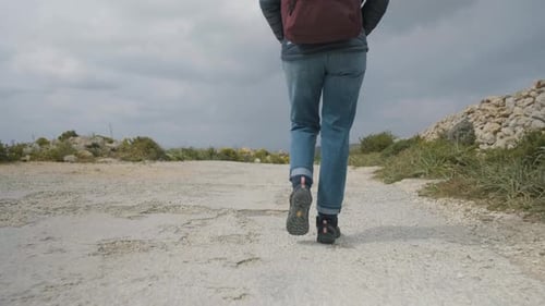 Close-up of the legs of a hiker walking on a rural road in the mediterranean nature on a cloudy win