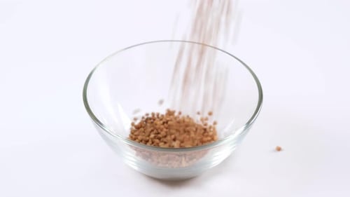 Buckwheat Grains Filling Glass Bowl on White Surface