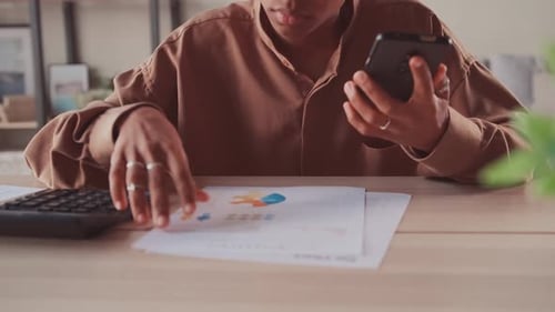 Analyst Reviews Charts with Phone and Calculator