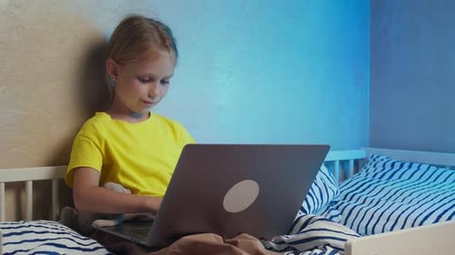 Child Uses Laptop Computer While Sitting in Bed