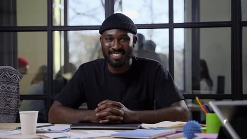 Smiling Man Sits at Desk in a Modern Office