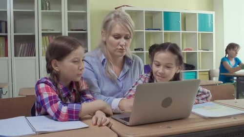 Teacher Helping Students with Laptop in Classroom