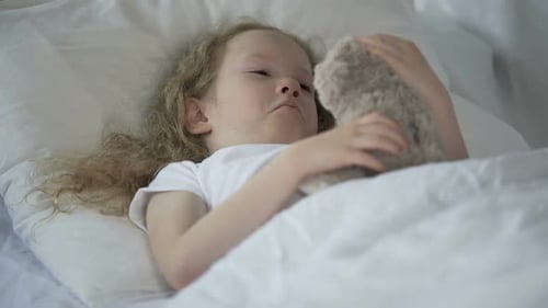 Child Sleeps Comfortably with Teddy Bear in Bed