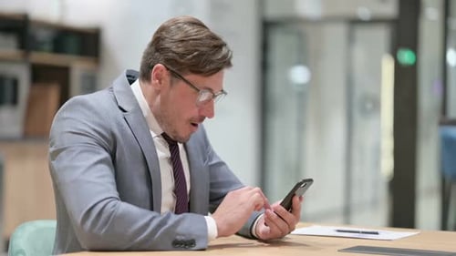 Businessman Celebrating Success on Smartphone in Office