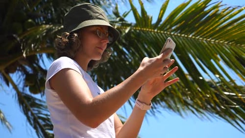 Young Woman In Summer Hat Using Mobile Phone At The Beach