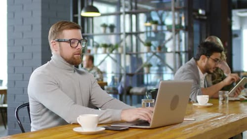 Caucasian Businessman Working on Laptop and Drinking Coffee in Cafe
