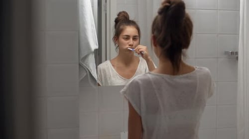 Young Woman Brushing Teeth in Bathroom Mirror