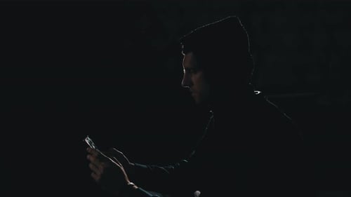 Silhouette of Man in Hood Scrolling News Feed on Smartphone.