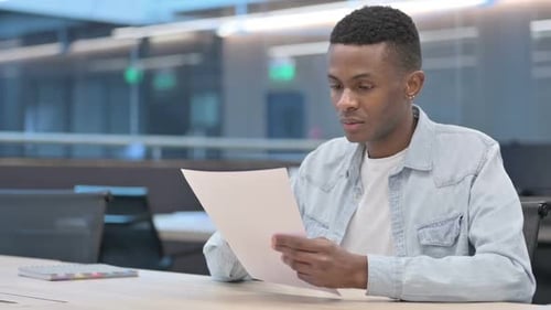 Young Adult Reviews Documents in a Modern Office