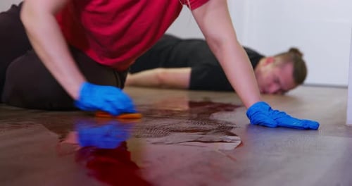 Una persona mató a un hombre y ahora intenta quitarse la mancha de sangre del piso de un apartamento con guantes de goma