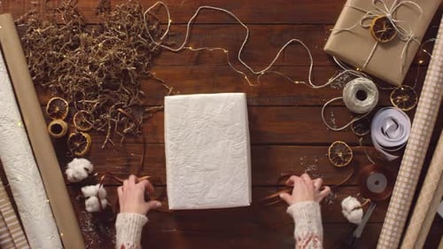 Person Wrapping Gift on Wood Table for Christmas