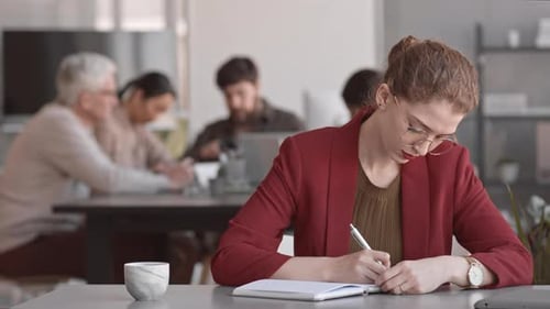 Focused Young Woman Writing at Office Desk