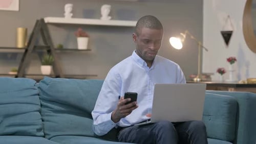 Young Adult Uses Phone and Laptop at Home
