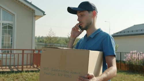 Delivery Worker Walking Outdoors Holding Package and Speaking on Mobile Phone