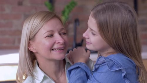 Glückliche Mutterschaft, kleines lächelndes Mädchen erzählt geliebte Mutter und flüstert zu Hause Geheimnisse ins Ohr