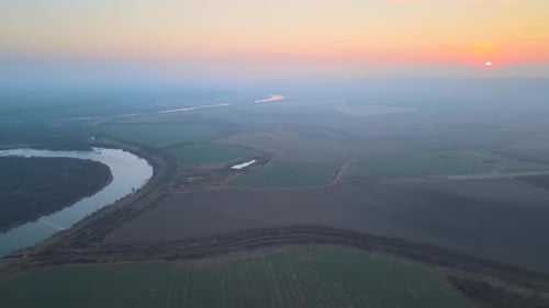 Luftaufnahme eines breiten Flusses, der am Herbstabend ruhig in der ländlichen Landschaft fließt