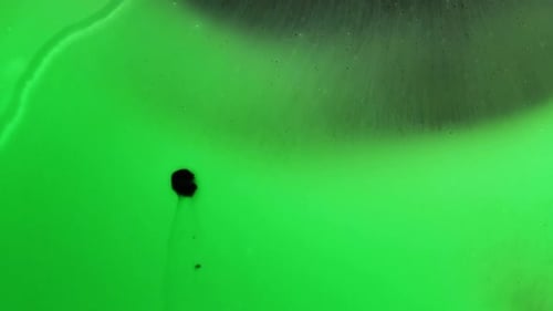 Macro top shot of green liquid which gets dissolved by black liquid. the black liquid covers the hol
