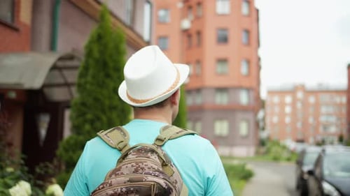 Man tourist in a hat and with a backpack travels through the city streets, camera tracking