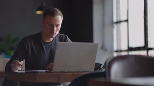Man Works at Laptop and Writes Notes Indoors