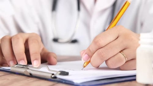 Female Doctor Hand Writing Prescription on Desk Close Up
