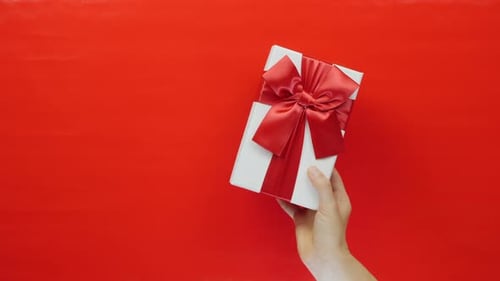 Arm Holds a Gift Box on Red Background
