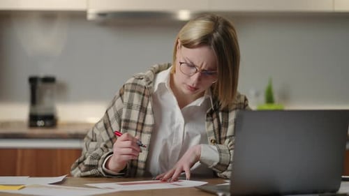 A Woman with Glasses Works Remotely From Home Sitting at a Table with a Laptop and a Felttip Pen