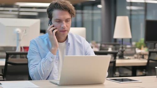Man Talking on Smartphone While Using Laptop in Office