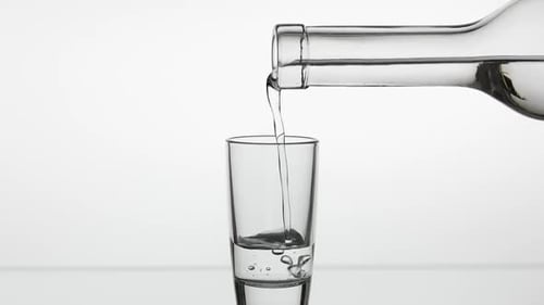 Pouring Up Shot of Vodka From a Bottle Into Glass. White Background
